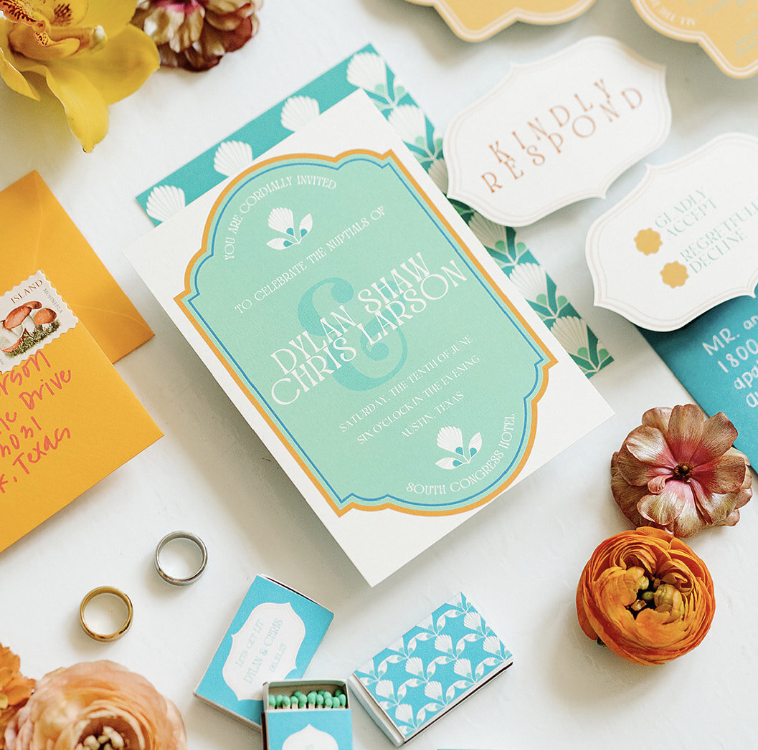 Colorful flat lay of wedding stationery suite including teal and orange invitation, RSVP cards, envelopes, and fresh floral accents.